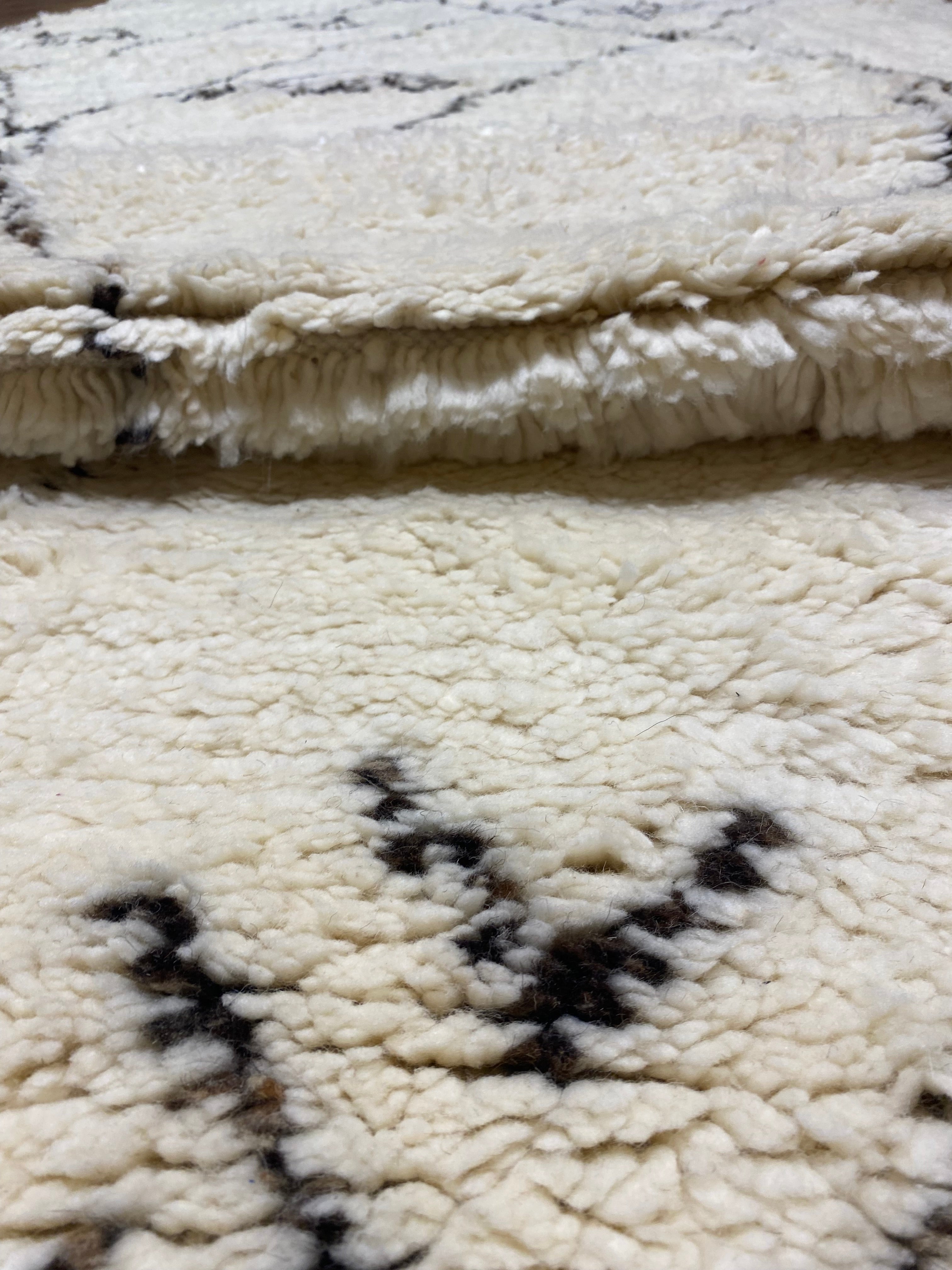Close-up of a cozy, thick Moroccan rug with a soft cream base and dark intricate patterns displayed on Santa Barbara Chic Moroccan product page.