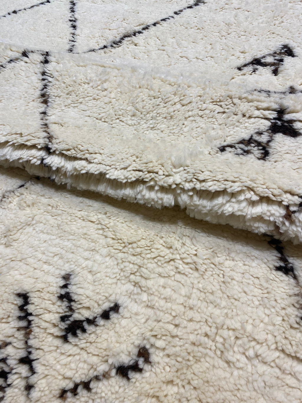 Close-up of a soft, textured Moroccan rug with geometric patterns in black on an off-white background.
