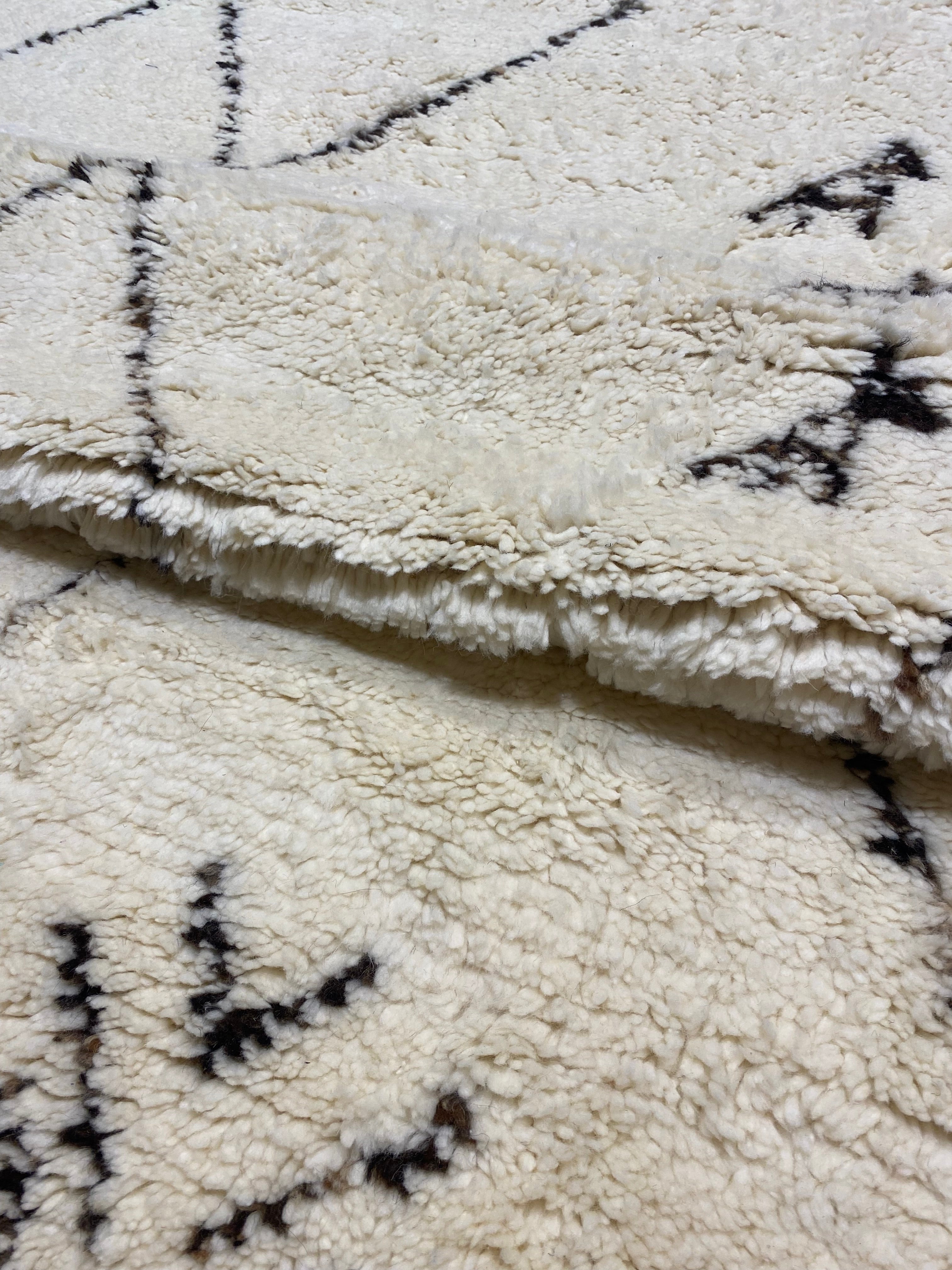 Close-up of a soft, textured Moroccan rug with geometric patterns in black on an off-white background.