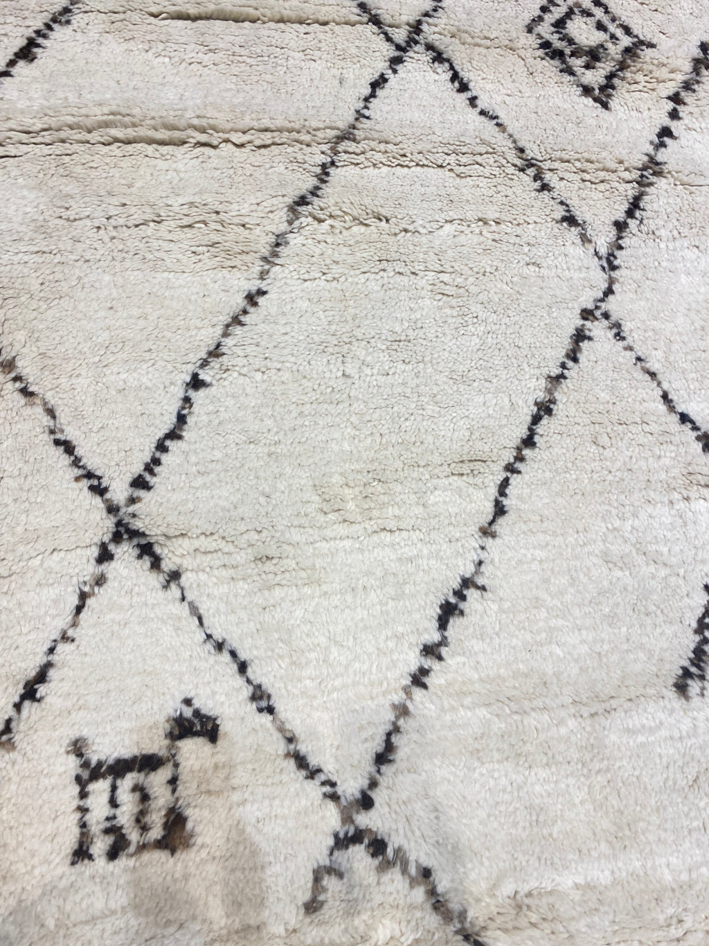 Santa Barbara Chic Moroccan rug with a beige background, black diamond-shaped patterns, and a small geometric figure in one corner.